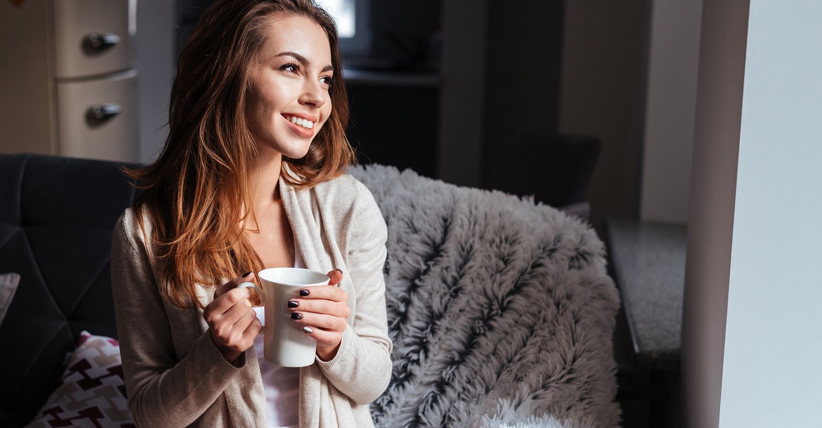 A smiling woman holding a mug of coffee at home